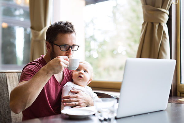 man with notebook in cafe sitting at the table drinking coffee, holding his son in his lap