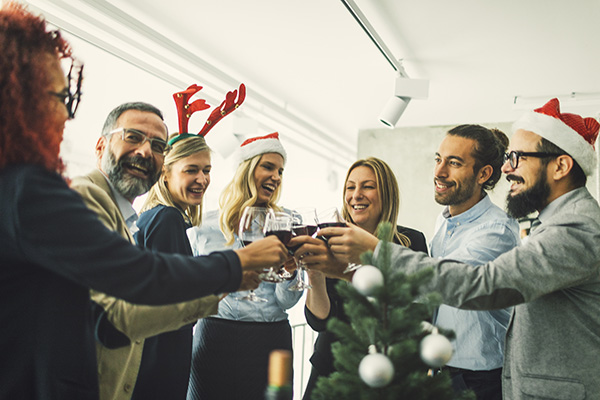 Business people celebrating Christmas At Workplace. Tosting with red wine. Wearing santa hat and reindeer headband.